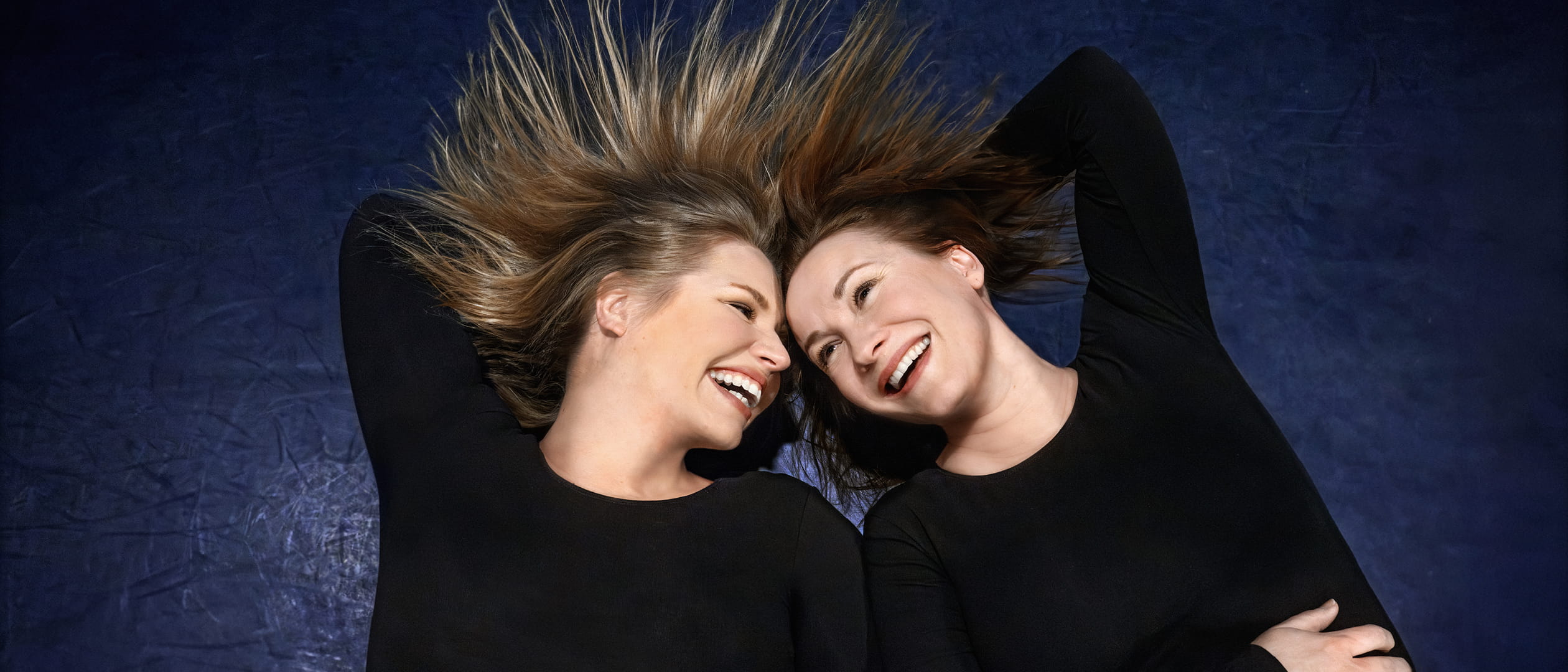 Affischbild för repertoaren Raka rör. Två kvinnor ler mot varandra.